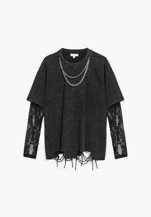 Camiseta negra de gran tamaño con mangas de encaje, dobladillo desgastado y cadena plateada colgando del escote; mezcla de algodón con acabado texturizado.