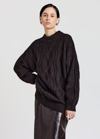 Dunkelbrauner Strickpullover mit hohem, umgeklapptem Kragen, der ein strukturiertes Wellenmuster und übergroße Ärmel aufweist. Getragen über einem glänzenden burgunderfarbenen Rock.