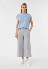 Helleblaue, kurzärmelige T-Shirt mit Textgrafik, kombiniert mit grauen, weiten Hosen. Das Modell trägt weiße Sneakers. Einfaches Design und weicher Stoff.