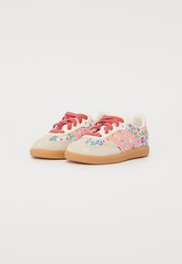 Pink and beige sneakers with floral patterns, featuring red laces and three pink stripes. Rubber sole with textured grip.