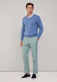 Maglione azzurro chiaro, camicia bianca con colletto, pantaloni verde menta e sneaker scure. Outfit casual con una vestibilità rilassata e linee pulite.