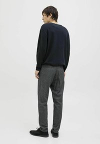 Czarna koszula z długim rękawem, szare, teksturowane spodnie i czarne buty. Skupienie na luźnym kroju i casualowym stylu. Neutralne tło.