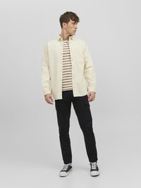 Light beige button-up shirt over a striped brown and white t-shirt, paired with black cargo pants and black sneakers.
