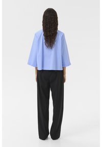 Light blue striped cropped shirt with wide sleeves, paired with black loose-fitting trousers. Plain design with a smooth texture.