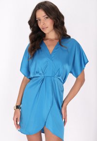 Rochie din satin de culoare albastră strălucitoare, cu mâneci scurte tip batwing, decolteu în V și un tiv asimetric, având detalii pliate la talie.