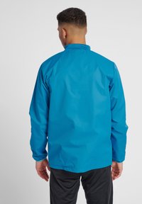 Blauwe lichtgewicht jas met een staande kraag, lange mouwen en elastische manchetten. Glad, waterdicht materiaal zonder zichtbare patronen of accenten.
