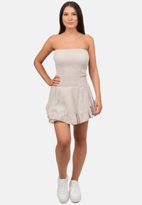 Lichtbeige strapless jurk met textuurstof, smock-bodice en gerimpelde zoom. Gecombineerd met witte sneakers voor een casual look.
