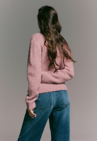 Maglione rosa peloso con scollatura rotonda, abbinato a jeans in denim blu a vita alta con tasche posteriori e una vestibilità comoda.
