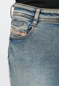 Μπλε τζιν παντελόνια με ξεθωριασμένο πλύσιμο, διαθέτοντας μια μικρή πίσω τσέπη με ετικέτα. Το ύφασμα έχει υφή με ορατές ραφές.