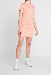 Růžové polo šaty s krátkými rukávy, přiléhavý střih, nařasení v pase, kombinované s bílými teniskami a ponožkami.