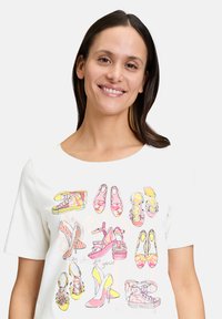 Weißes Baumwoll-T-Shirt mit bunten Schuhillustrationen in Pink, Gelb und Orange. Rundhalsausschnitt, kurze Ärmel und lockere Passform.