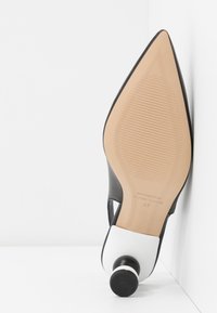 Chaussure à talon haut à bout pointu noir et blanc avec semelle beige texturée et talon empilé rond noir et blanc, vue côté semelle.