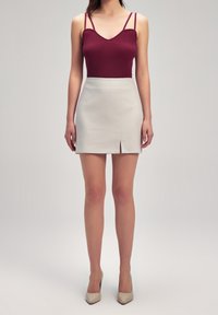 Burgundy rippad linne med tunna remmar som matchas med en krämfärgad minikjol med en framslits, avslutad med beige spetsiga klackar.