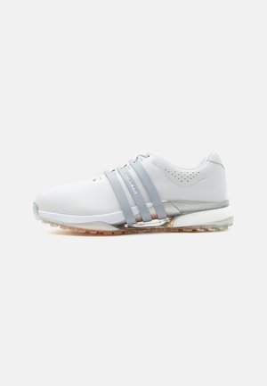 Λευκό αθλητικό παπούτσι με τρεις γκρι λωρίδες στο πλάι, τρύπες κοντά στη φτέρνα, υφή στη σόλα και αντανακλαστική λεπτομέρεια στη μέση της σόλας, σε λευκό φόντο.