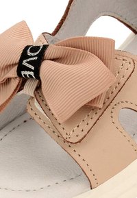 Béžové sandály s texturovanou mašlí a černou akcentovou visačkou. Vyrobené z kůže s měkkou, světle šedou stélkou a šitými detaily.