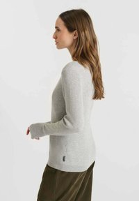 Light gray ribbed sweater with long sleeves, fitted design, and a side tag detail. Worn with a textured olive green skirt.