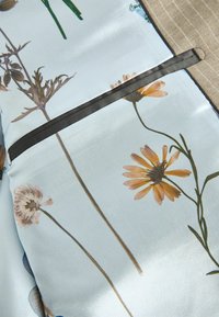 Blumenmusterstoff in Hellblau mit glatter Oberfläche, verfügt über braune Nähte und ein dunkles Akzentband über dem Design.