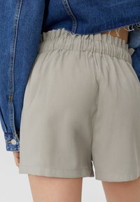 Shorts légers beiges avec une taille élastique, présentant une texture lisse et un ourlet arrivant au-dessus du genou, associés à une veste en denim bleu.
