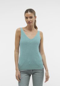 Lichtgroene mouwloze top met een diepe V-hals, geribbelde textuur en een aansluitend ontwerp. Gecombineerd met lichtblauwe jeans voor een casual uitstraling.