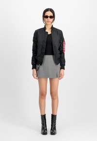 Svart bomberjakke med glidelås og rød tag, kombinert med en ribtstrikket grå miniskjørt og knelang svarte støvler. Modellen har på seg solbriller.