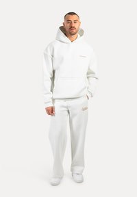 Hoodie blanc avec poche avant et logo brodé, associé à un pantalon de jogging assorti. Matière douce, coupe décontractée et poignets côtelés.