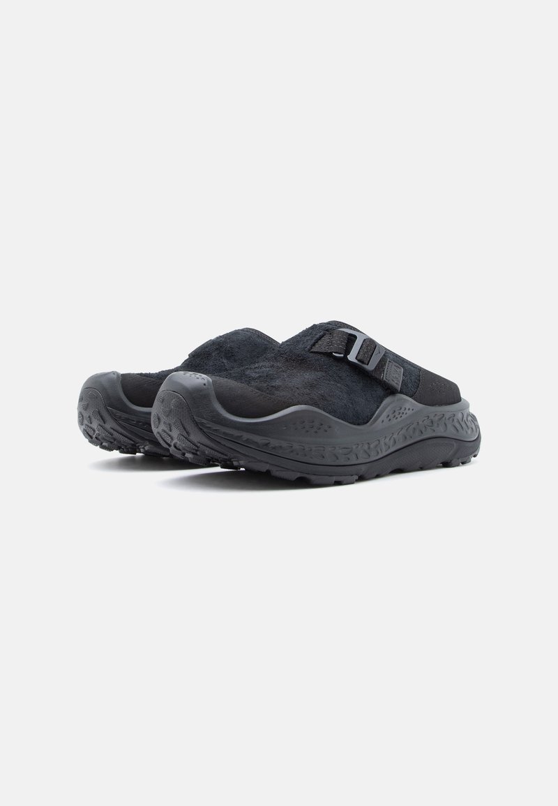 Svarta skor med en strukturerad mockaöverdel och en tjock, mönstrad gummisula. Har ett band över toppen för säker passform.