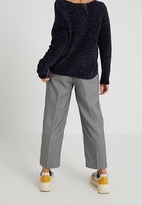 Granatowy sweter dziergany o luźnym kroju, zestawiony z czarno-białymi spodniami w pepitkę. Obuwie posiada żółty akcent.