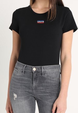 Kobieta ubrana w czarny t-shirt Levi's z małym logo na piersi oraz szare, podarte jeansy z wysokim stanem.