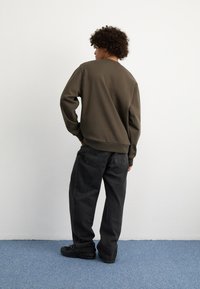 Sudadera verde oliva con un corte relajado, combinada con vaqueros negros holgados. La tela parece suave y los pantalones tienen un diseño clásico de cinco bolsillos.