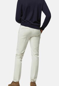 Ljusbeiga byxor med slim fit, med en bakficka med en diskret dragkedjedetalj, matchade med en marinblå tröja.