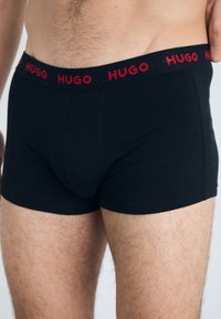 Boxers en coton noirs avec ceinture rouge "HUGO". Le design présente une coupe ajustée avec une texture lisse et des détails cousus.