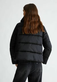 Giubbotto puffa nero con colletto alto e design a righe orizzontali. Realizzato in tessuto liscio, presenta una vestibilità corta e cuciture minime.