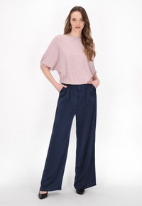 Top rosa chiaro, lavorato a maglia morbida con scollo ampio; pantaloni blu navy plissettati a gamba larga; indossato con tacchi a punta neri.