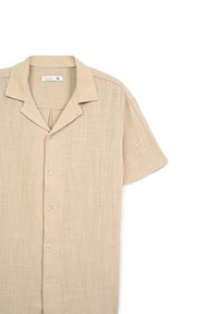 Camicia beige a maniche corte con tessuto testurizzato, abbottonatura frontale e colletto a punta. Presenta cinque bottoni di colore chiaro e una vestibilità rilassata.
