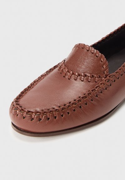 Mocassin en cuir marron avec surpiqûres décoratives le long de l'embout et des côtés, semelle plate, présenté sur fond blanc.