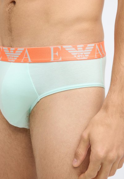 Cuecas verdes menta claras com um cós elástico laranja apresentando um logótipo. O tecido parece suave, sem padrões ou detalhes visíveis.