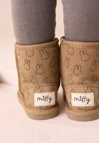 Beige Wildlederstiefel mit einem wiederholten Hasenmuster, weicher Textur, runder Form und einem weißen Etikett mit der Marke "miffy".