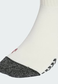 Calza bianca con un corpo a maglia testurizzata e una zona della punta grigio scuro. Presenta una cucitura del logo rosso vicino alla caviglia. Tessuto liscio in tutto il resto.
