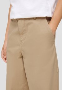 Beige Hosen aus leichtem Stoff mit glatter Textur, ausgestattet mit Seitentaschen und flachem Frontdesign.