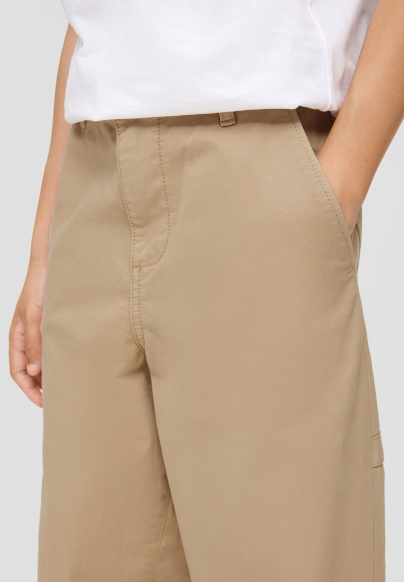 Beige Hosen aus leichtem Stoff mit glatter Textur, ausgestattet mit Seitentaschen und flachem Frontdesign.