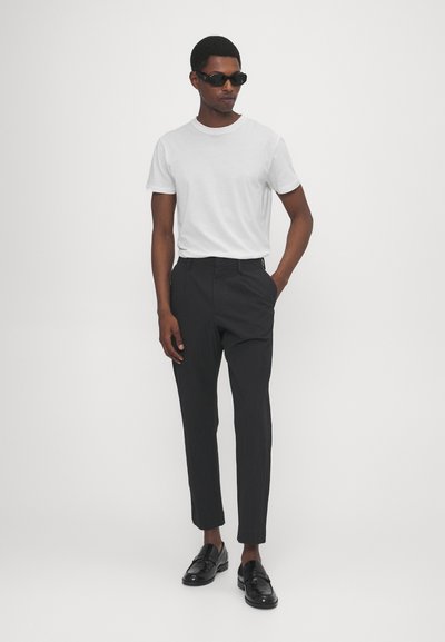 Vit bomull t-shirt som matchar mörka, randiga skräddarsydda byxor. Svarta slip-on skor fulländar looken, med mörka solglasögon som accent.