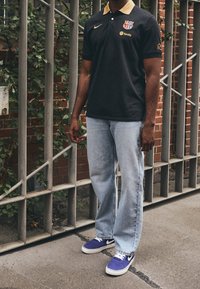 Czarna koszulka polo z złotymi akcentami, z logo, w połączeniu z jasnoniebieskimi dżinsami o prostym kroju i fioletowymi sneakersami Nike.