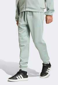 Light green athletic pants with a slight texture, featuring an elastic waistband and side pockets, paired with black sneakers and white accents.