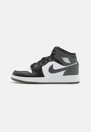 Schwarzer, weißer und grauer High-Top Nike Air Jordan Sneaker mit Schnürsenkeln, Swoosh-Logo und Wings-Logo am Knöchelkragen, Seitenansicht auf weißem Hintergrund.