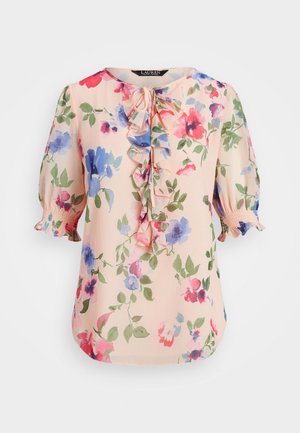 Blouse rose clair à imprimé floral rouge, bleu et violet, avec un col noué à volants sur le devant et des manches courtes bouffantes avec poignets élastiques.