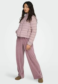 Hele lilla puffjakk, millel on kõrge krae ja horisontaalsed õmblused, koos laiadest jalgadest pehmeate matching pükstega ja pruunide kingadega.