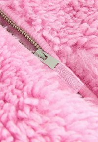 Roze textiel met een fluffy uitstraling, voorzien van een zilveren rits langs de rand en een zachte, tactile oppervlakte.