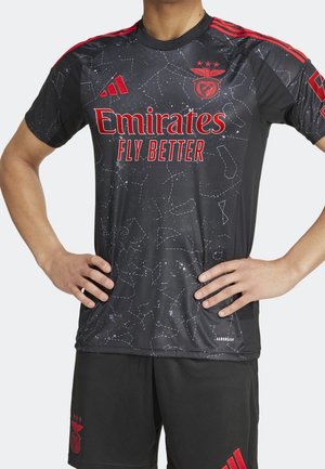 Mann trägt ein schwarz-rotes Benfica-Fußballtrikot und Shorts mit dem Sponsor "Emirates Fly Better" und einem Sternbildmuster auf dem Trikot.