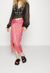 Top nero trasparente a maniche lunghe con ricami floreali, abbinato a una gonna avvolgente a fantasia floreale rosa e sandali neri con tacco chunky.