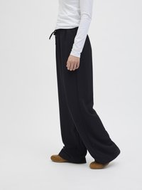 Pantalons noirs à jambes larges avec une taille élastique à cordon de serrage, associés à une chemise blanche ajustée à manches longues et des pantoufles marron. Texture lisse.